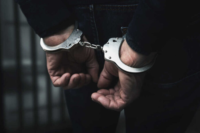 Arrested,Man,With,Cuffed,Hands,Behind,Prison,Bars