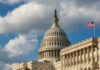 The U.S. Capitol building with a dome and an American flag under a cloudy sky