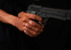 Close-up of a hand holding a black handgun against a dark background