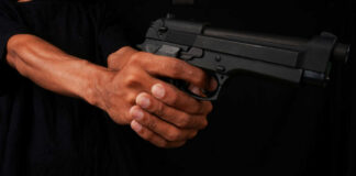 Close-up of a hand holding a black handgun against a dark background