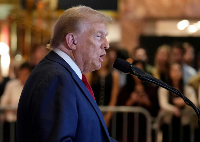 A public figure speaking into a microphone with an audience in the background