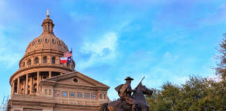 Statue of a rider in front of the Texas State Capitol building under a blue sky