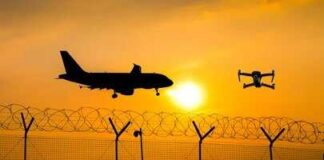 An airplane and a drone flying against a sunset backdrop with a barbed wire fence