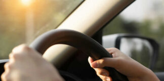 Hands gripping a steering wheel inside a car with sunlight streaming in