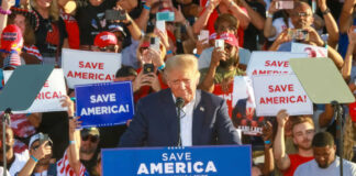 Donald Trump speaking at a political rally with supporters holding signs