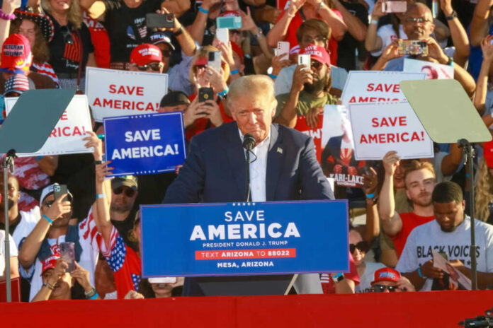 Donald Trump speaking at a political rally with supporters holding signs