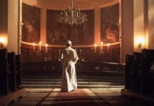 A religious figure standing in a church with candlelight and historic artwork