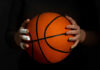 Hands with bandages holding an orange basketball against a dark background