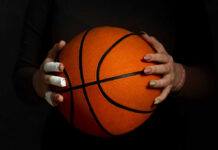 Hands with bandages holding an orange basketball against a dark background
