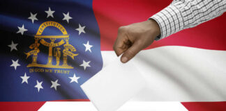 A hand placing a ballot into a ballot box with the Georgia state flag in the background