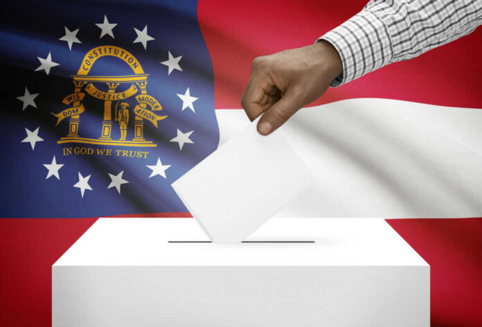 A hand placing a ballot into a ballot box with the Georgia state flag in the background