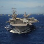An aircraft carrier surrounded by various naval ships in the ocean