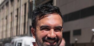 A smiling man in a casual white shirt standing outdoors