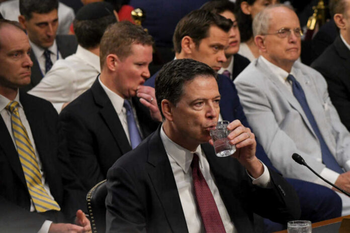 A man in a suit drinking water during a congressional hearing