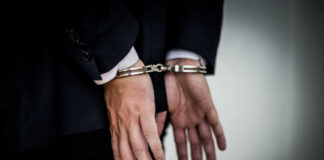 A person in a suit with hands cuffed behind their back