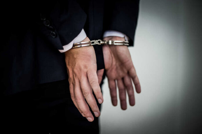 shutterstock_702901249.jpg A person in a suit with hands cuffed behind their back