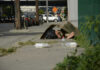 A person lying on the sidewalk under a cardboard box in an urban setting