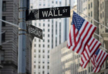 Street signs for Wall Street and Broad Street with American flags in the background