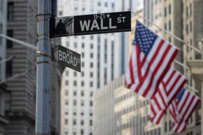 Street signs for Wall Street and Broad Street with American flags in the background