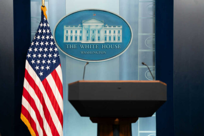 Podium with microphones in front of the White House seal and an American flag