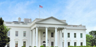 The White House with an American flag flying above, surrounded by greenery