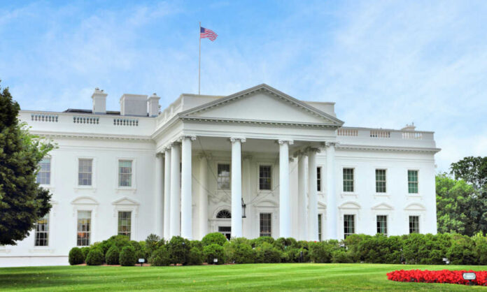 The White House with an American flag flying above, surrounded by greenery