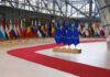 EU Pushback Surge: 120,000 Migrants Rejected! Flags of European countries displayed in a modern hall with a red carpet