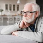 Elderly man with glasses resting his chin on his hand, looking thoughtfully