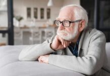 Elderly man with glasses resting his chin on his hand, looking thoughtfully