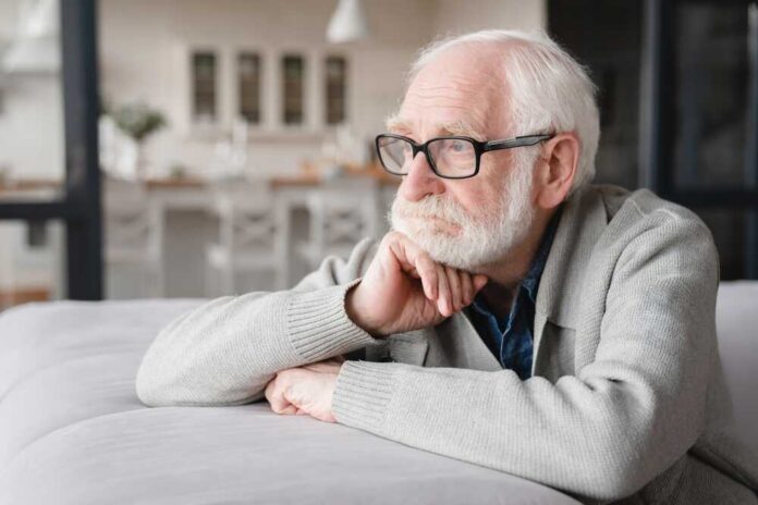 Elderly man with glasses resting his chin on his hand, looking thoughtfully