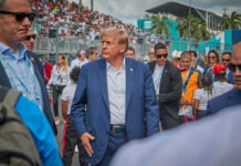 A man in a blue suit walking through a crowded outdoor event with security personnel