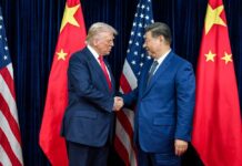 Two political leaders shaking hands in front of national flags