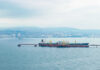 Oil tanker docked at a shipping port with a coastal city in the background
