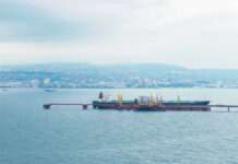 Oil tanker docked at a shipping port with a coastal city in the background