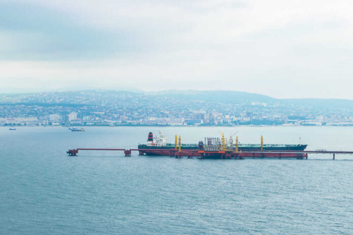 Oil tanker docked at a shipping port with a coastal city in the background