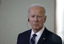 A serious-looking man in a suit with an earpiece, standing indoors