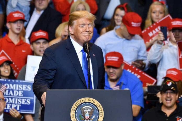 A speaker at a political rally smiling in front of an enthusiastic crowd wearing red hats