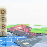 Debt Crisis Looms: Households Drowning Stack of wooden blocks spelling DEBT on top of various credit cards