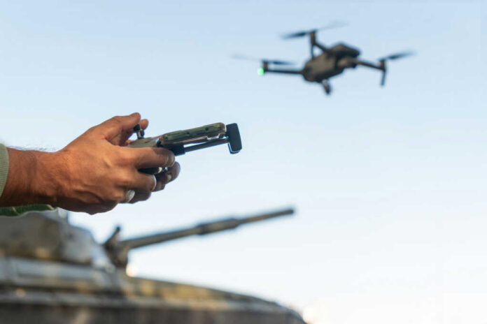 shutterstock_2430538153 Person controlling a drone with a remote while a tank is in the background