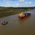 A cargo ship being assisted by a tugboat in a canal