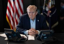MASSIVE Camp David Meeting—What’s the Real Agenda? A serious-looking man seated at a table with phones and an American flag in the background