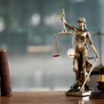 A bronze statue of Lady Justice holding scales and a sword, with law books and a gavel in the foreground