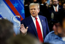 A man in a suit with a red tie speaking at a political event