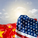 Crumpled flags of the United States and China against a cloudy sky
