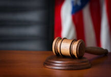Court Crackdown Exposes Biden Recordings A wooden gavel resting on a round base with a blurred American flag in the background