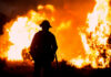 Silhouette of a firefighter standing in front of a large wildfire