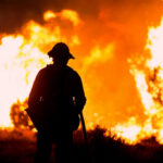 Wind-Whipped Monster Fire Baffles Officials Silhouette of a firefighter standing in front of a large wildfire