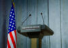 Israel Strikes Rattle Fragile Truce Press podium with microphones and American flag in the background