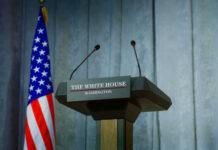 Israel Strikes Rattle Fragile Truce Press podium with microphones and American flag in the background