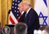 Donald Trump and another official at a press conference with flags in the background